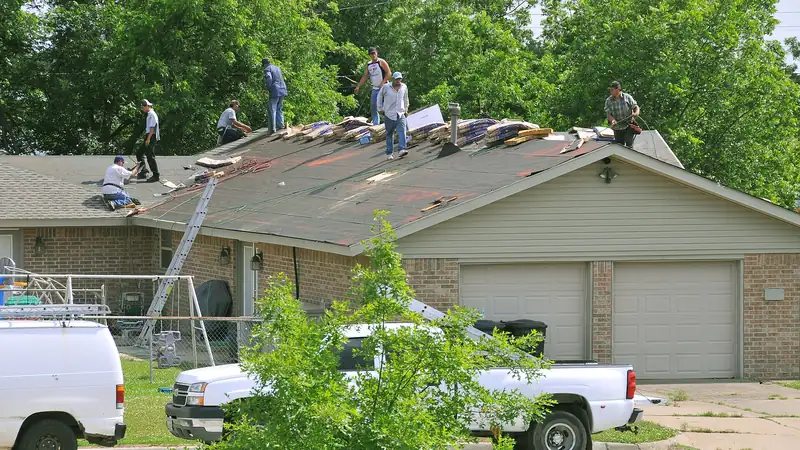 Roofing crew tearing off and replacing asphalt shingles on a one-story house